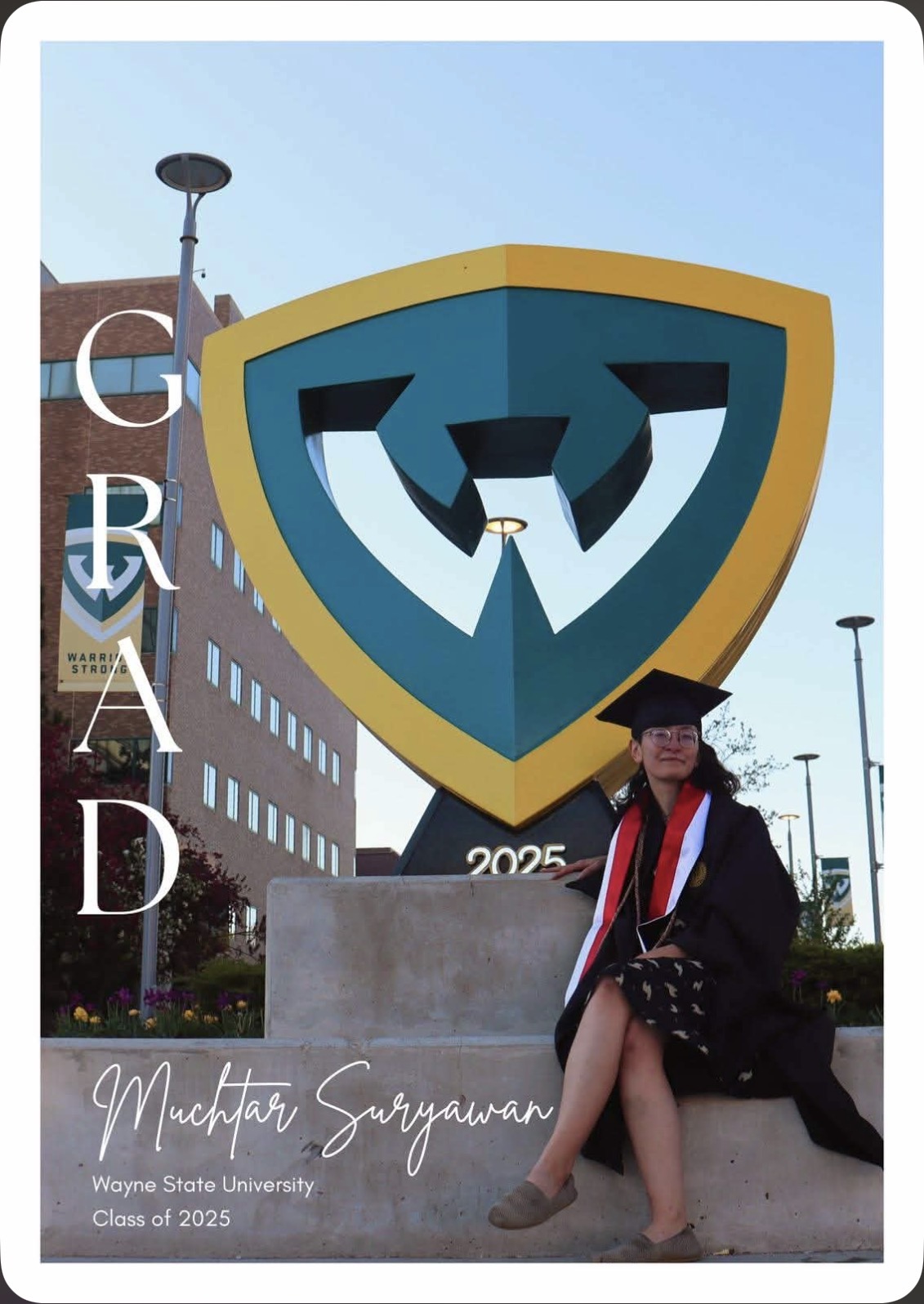 Muchtar in cap and gown by the Wayne State W sculpture, Class of 2025